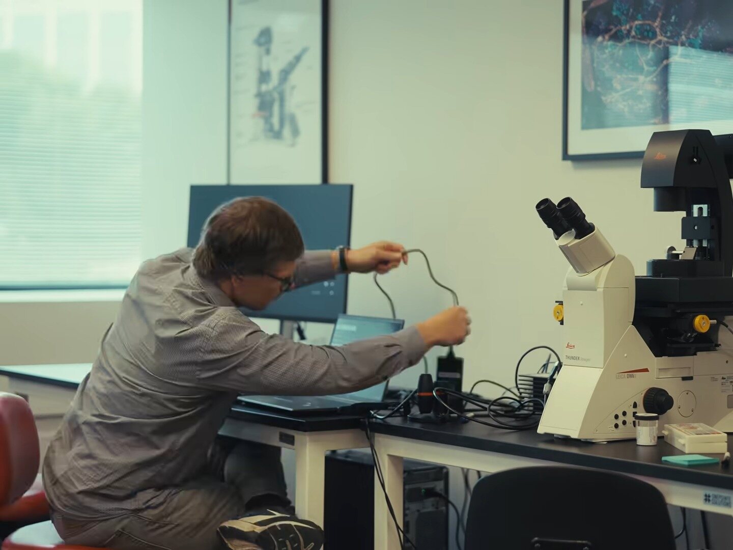 A scientist at a desk beside a microscope